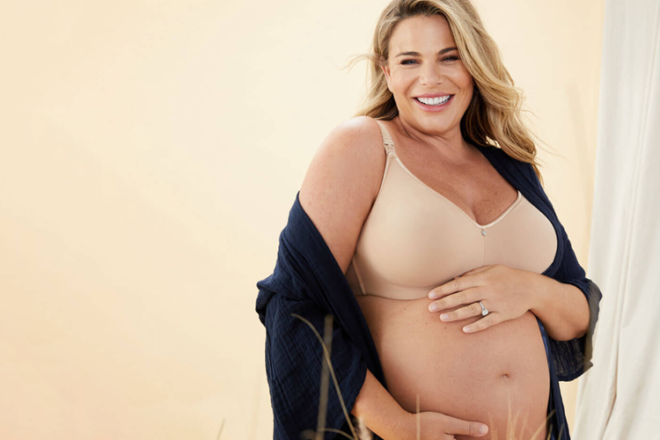 Femme enceinte souriante touchant le ventre portant un soutien-gorge d'allaitement Cake Maternité, montrant une vue de face des bonnets et de la sangle lisses et sans armatures.