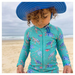 Jeune garçon à la plage portant un maillot de bain Purebaby pour jeunes, montrant le style et les imprimés pour filles et garçons, ainsi qu'un chapeau assorti.