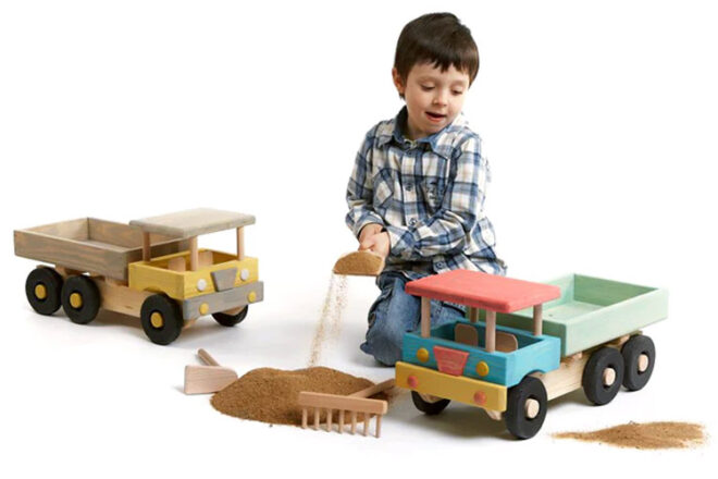 jeune garçon jouant avec du sable et de grands camions jouets en bois