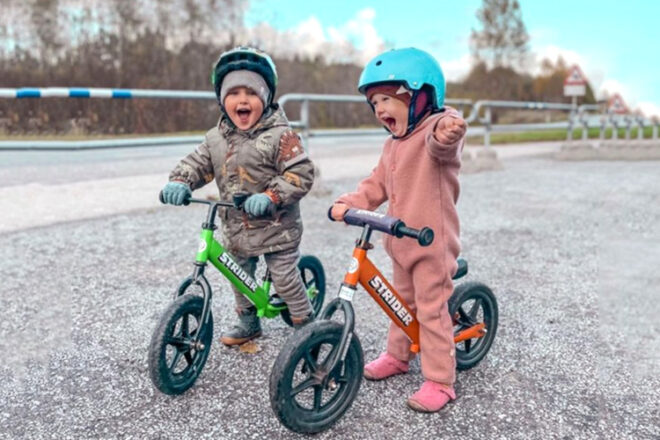 deux jeunes enfants assis sur un vélo d'équilibre strider un vert et un orange