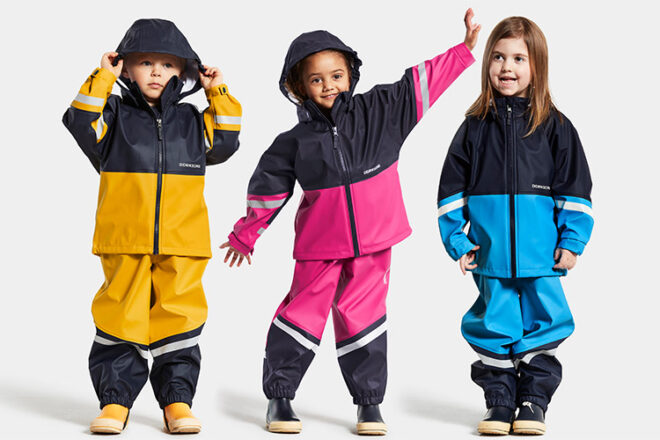 Trois enfants côte à côte portant des imperméables Didriksons pour tout-petits montrant les différentes couleurs et styles disponibles.