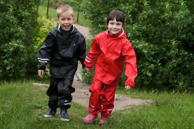Deux enfants se tenant la main et portant des vêtements de pluie Elka noirs et rouges assortis montrant la coupe et le style des vestes de pluie.