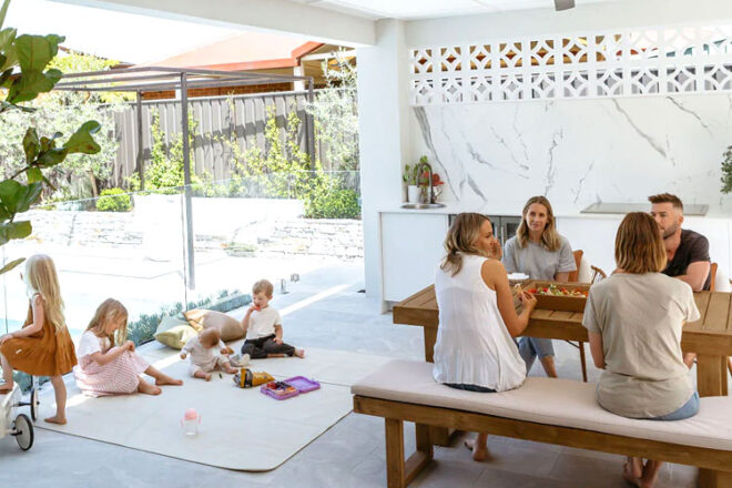 Tapis de pique-nique léger en cuir végétalien Henlee montrant des enfants et des bébés mangeant sur la surface résistante, avec des adultes assis à une table à proximité. 